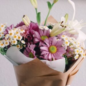 Elegant bouquet featuring purple daisies, white lilies, and delicate flowers wrapped in brown paper.
