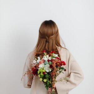 Back view of a woman holding a vibrant bouquet of mixed flowers against a white background.